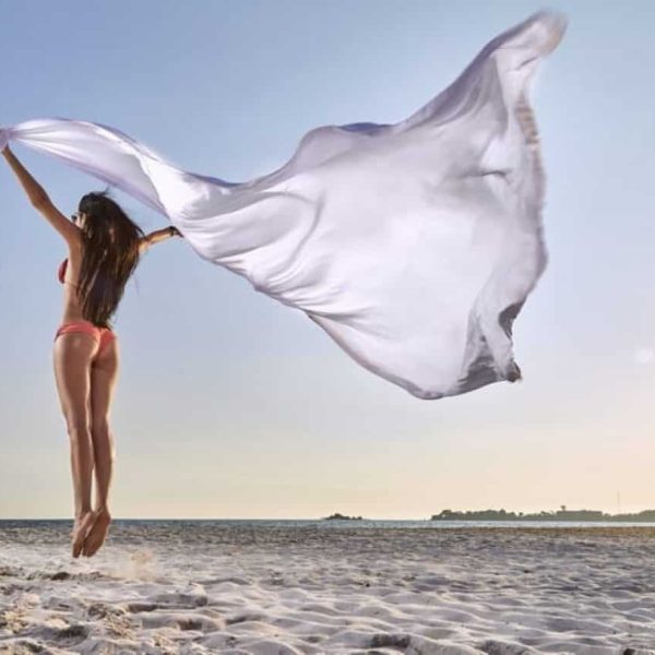 a woman in a garment jumping on a beach with a white fabric